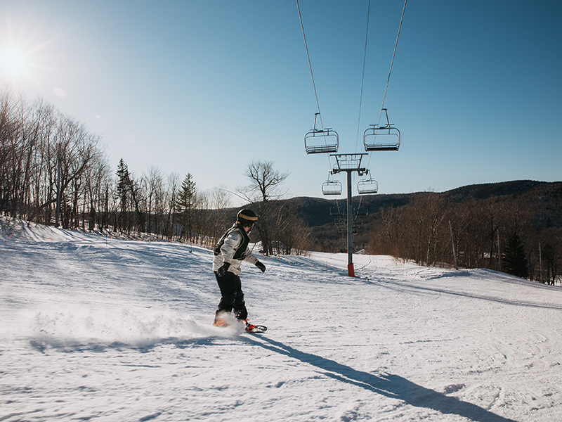 A chill youth snowboarding down a hill with the chairlift in the background