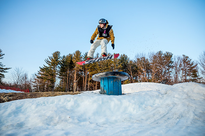A youth on a snowboard jumping over a wire spool.