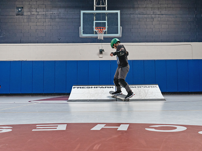 A Chill youth riding a skateboard on a ramp setup on a basketball court.
