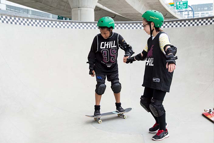 Chill youth helping another learn to ride inside a bowl