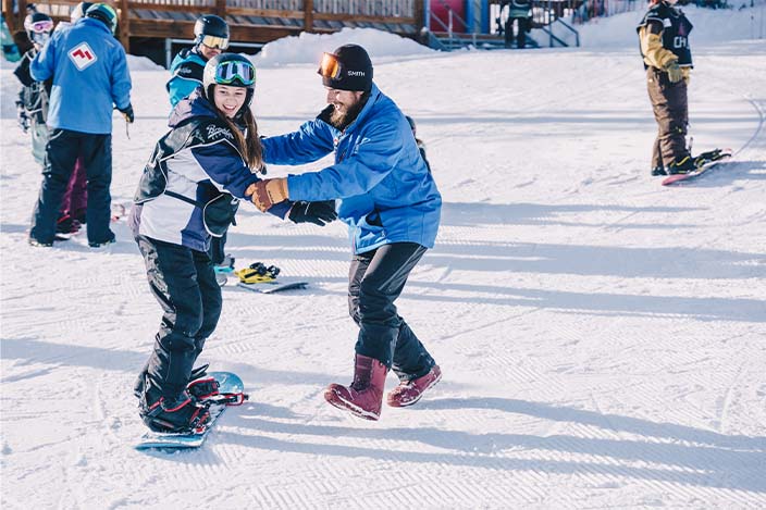 Snowboard instructor is holding hands of Chill youth while she learns to snowboard with a big smile