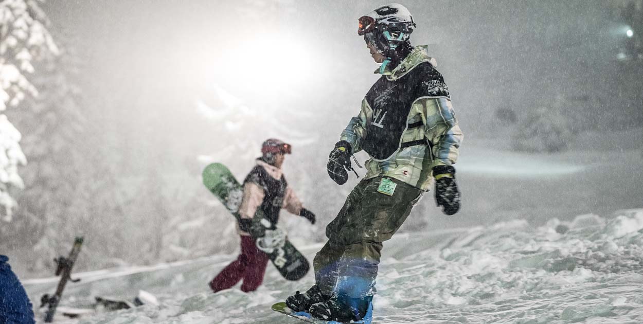 Chill youth snowboarding in the evening with snow falling around him