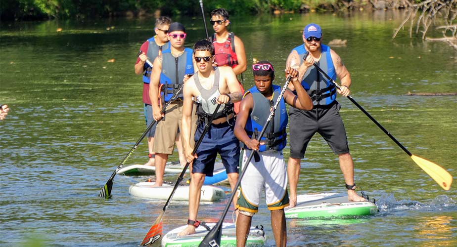 Group of Chill youth on a green river paddlebaording in a single file line