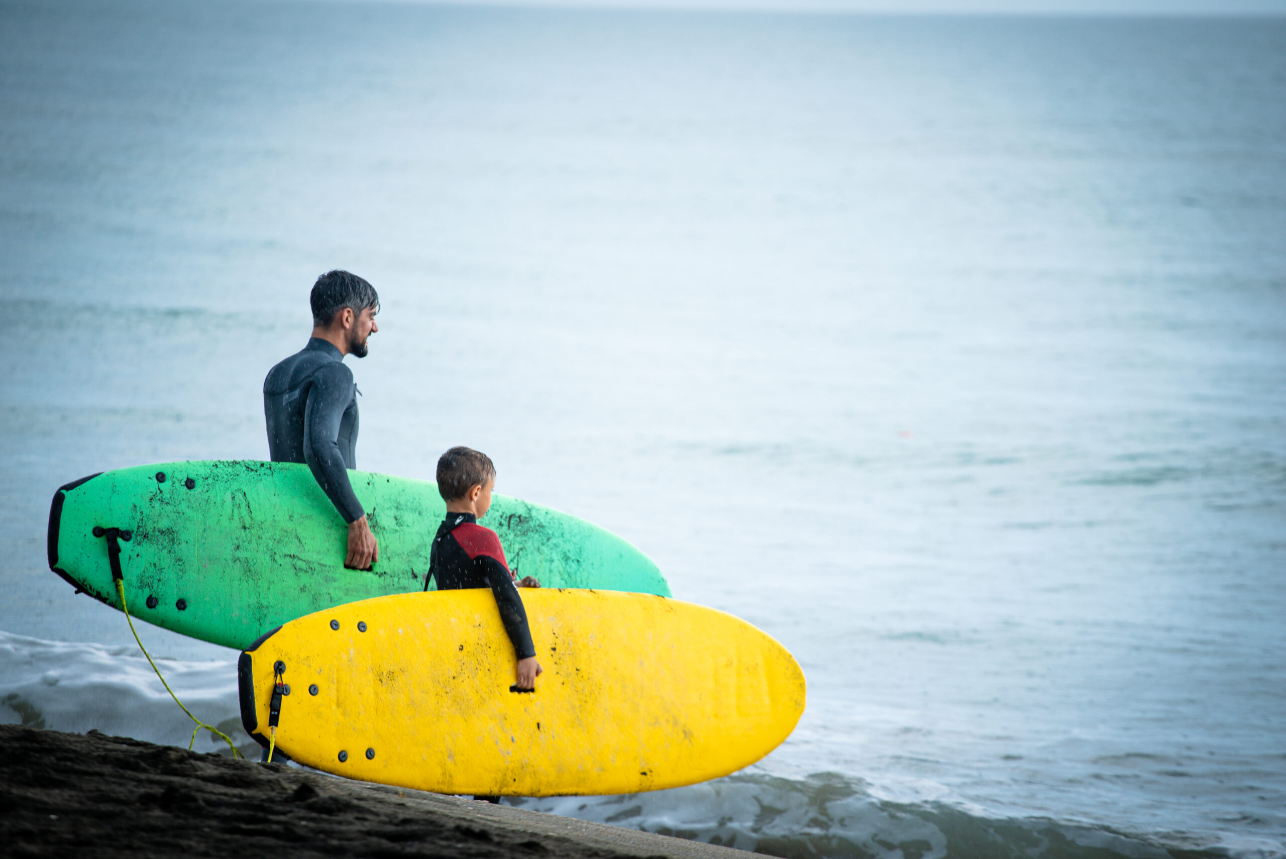 A Chill youth and mentor standing on the beach holding their surf boards.
