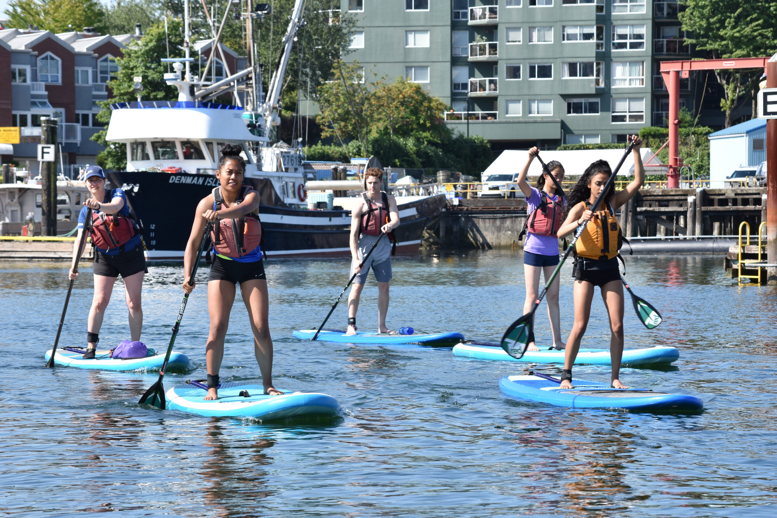 Chill youth and program coordinator paddleboarding with boats in the background.