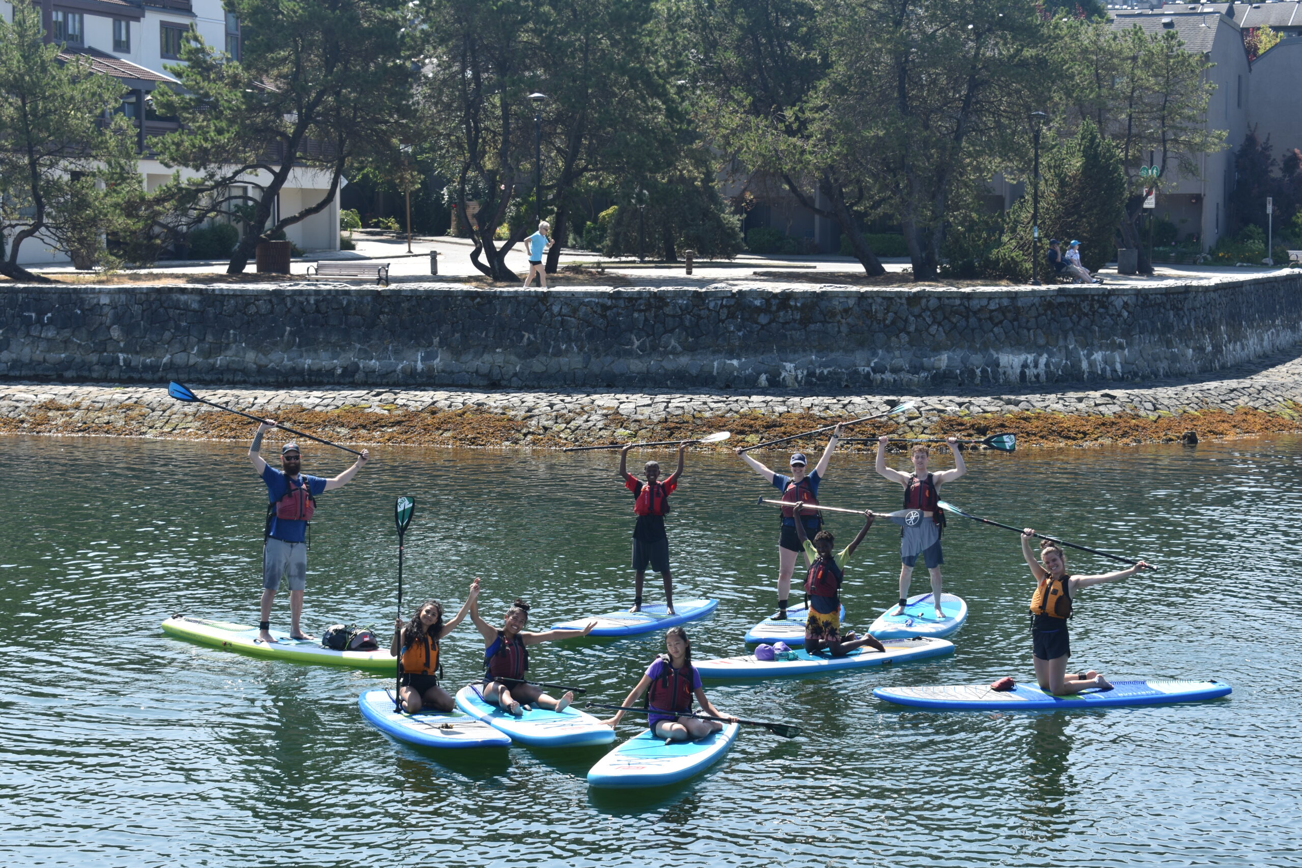 A whole group of Chill youth and adults on sup boards, posing for the photo with their paddles held in the air.