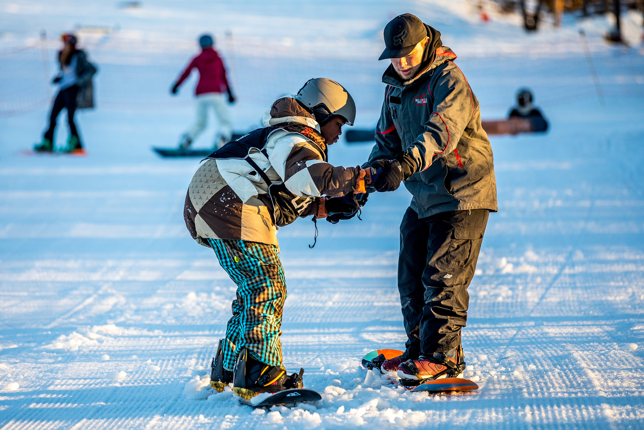 An instructor helps a Chill youth on their snowboard