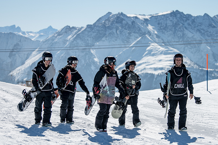 A group of Chill youth and an instructor carrying their snowboards in the Alps/