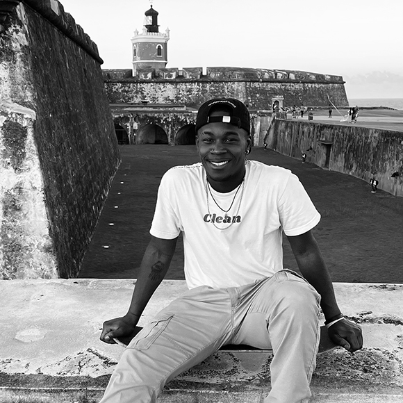 A picture of a man seated in front of a historical building.